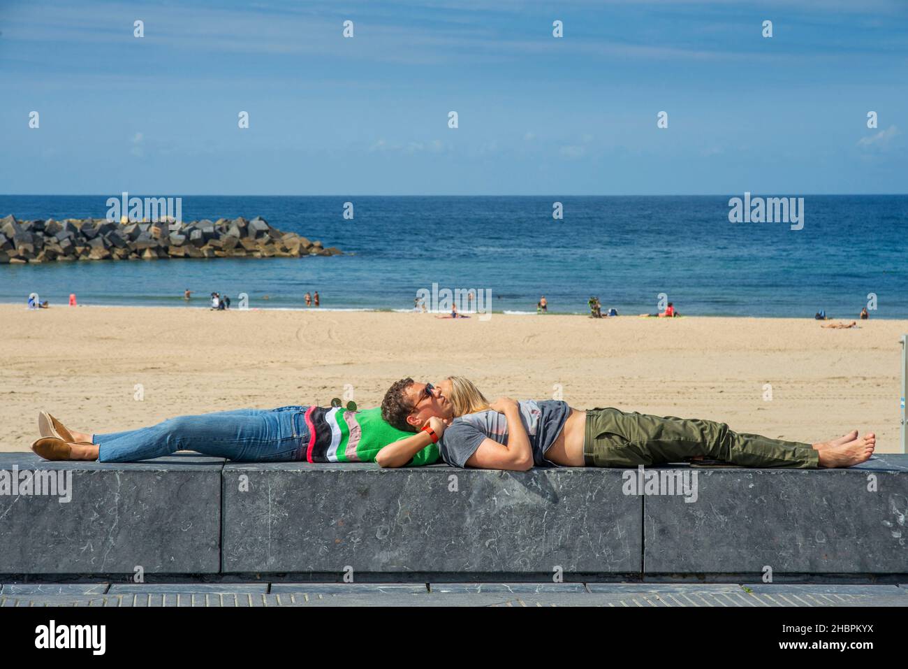 A romantic couple in A view of the beautiful but crowded Playa de La Concha (Beach of Zurriola) in San Sebastián (Donostia), Spain.  Beach of Playa de Stock Photo