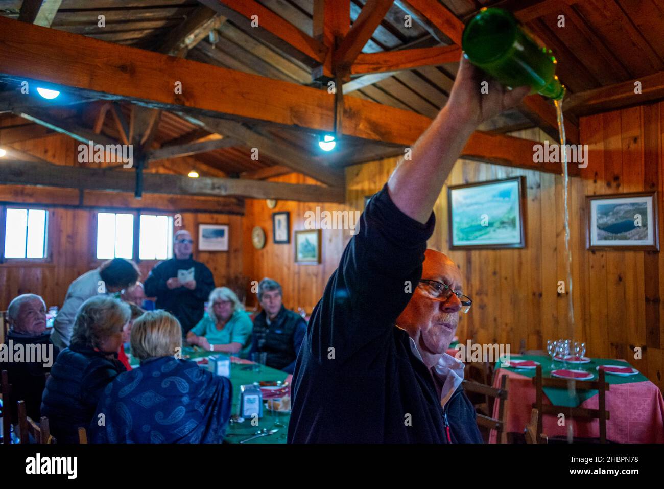 A Spanish waiter pouring cider or sidra from a bottle into a glass the traditional way in a sideria in El Casin restaurant in Picos de Europa, Parque Stock Photo