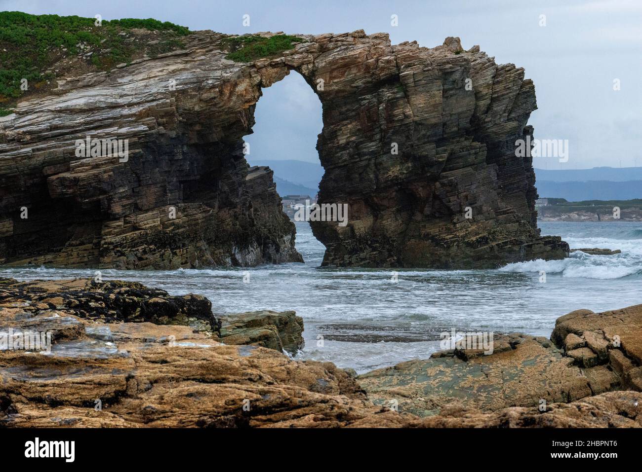 As Catedrais or Las Catedrales Beach by sunset, in Ribadeo, Lugo. Galicia, Spain. Tourists by a stone arch at Beach of the Cathedrals Natural Monument Stock Photo