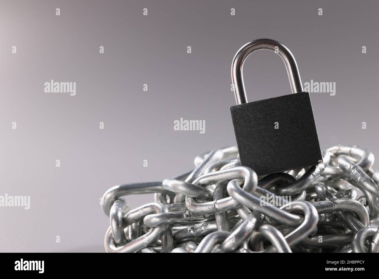 Solid metal locked padlock on top of tangled silver chain Stock Photo