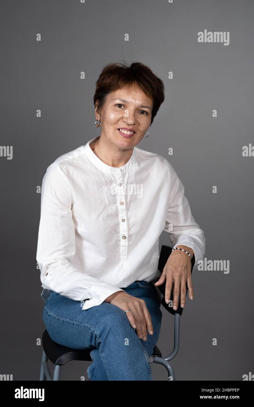 Portrait of elegant mature woman in white blouse sitting on chair and ...