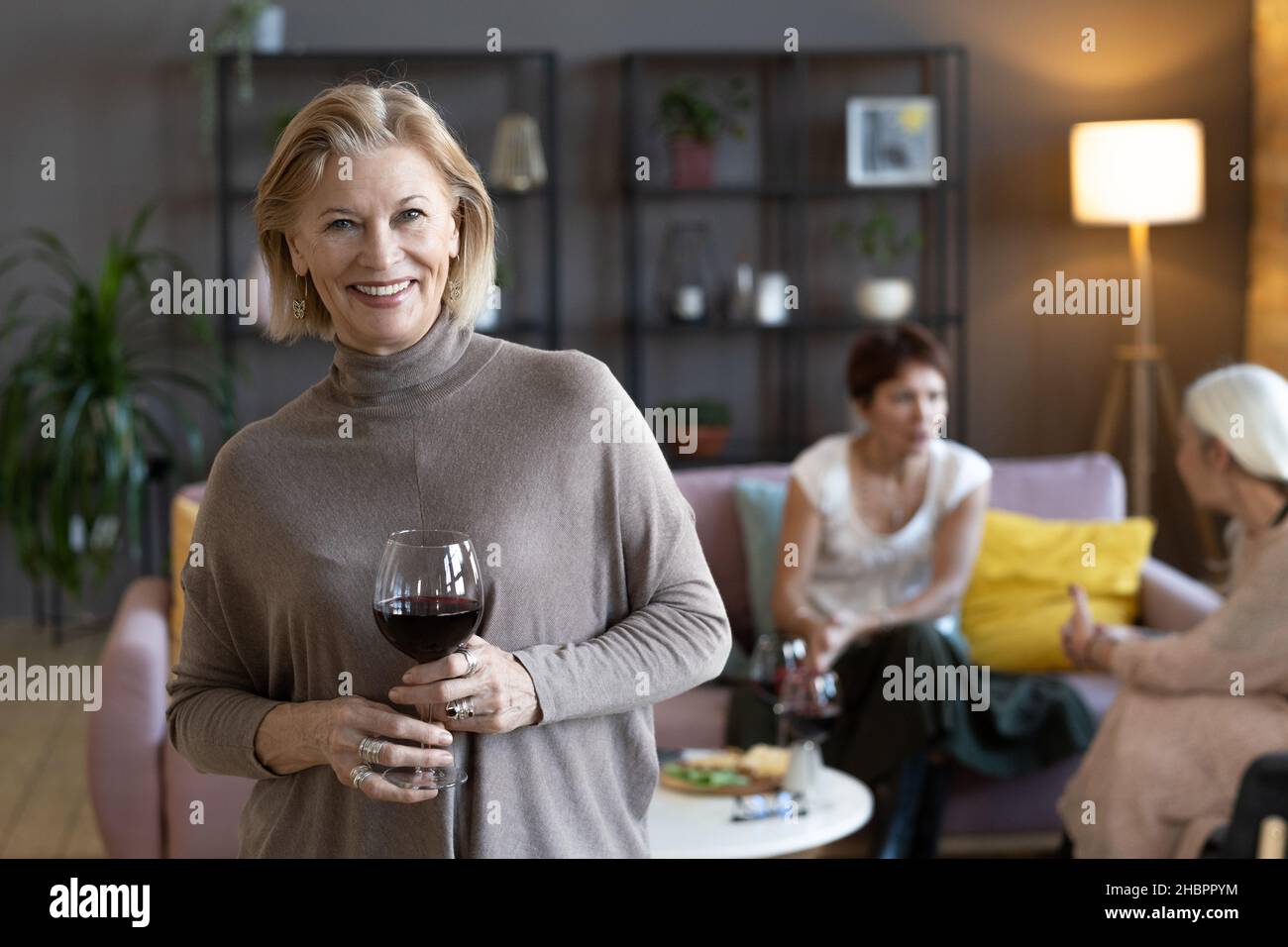 Portrait of mature woman holding glass of red wine and smiling at ...