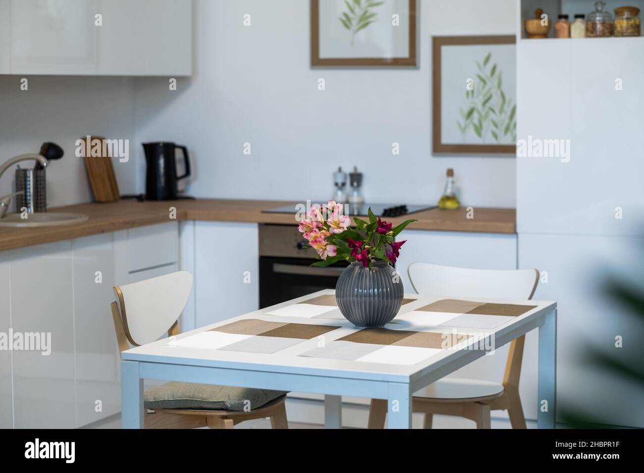 Image of beautiful flowers in vase on the kitchen table in empty domestic kitchen Stock Photo