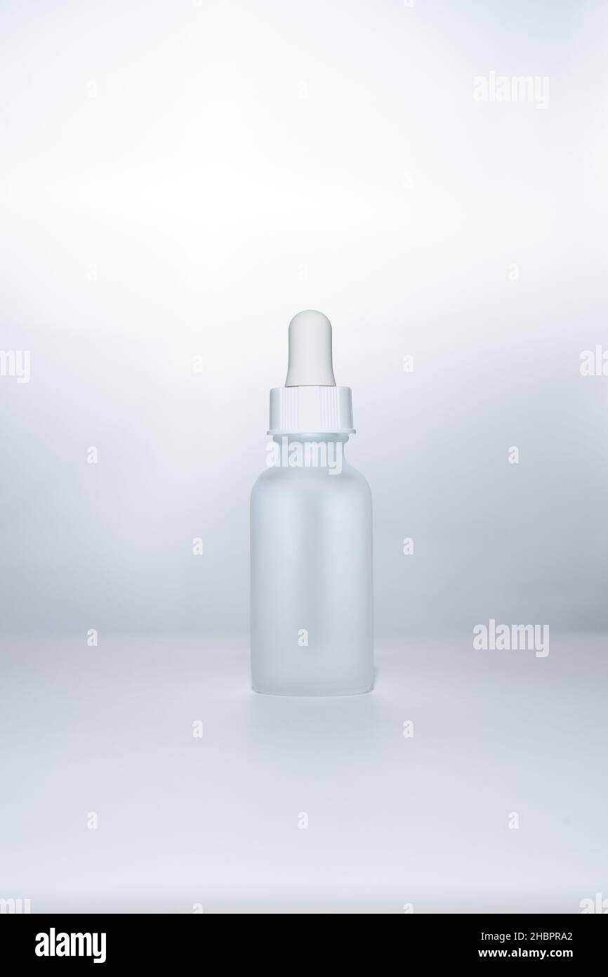 Light backlit face serum in white matte glass bottle with dropper. Anti aging facial liquid with peptides and collagen Stock Photo