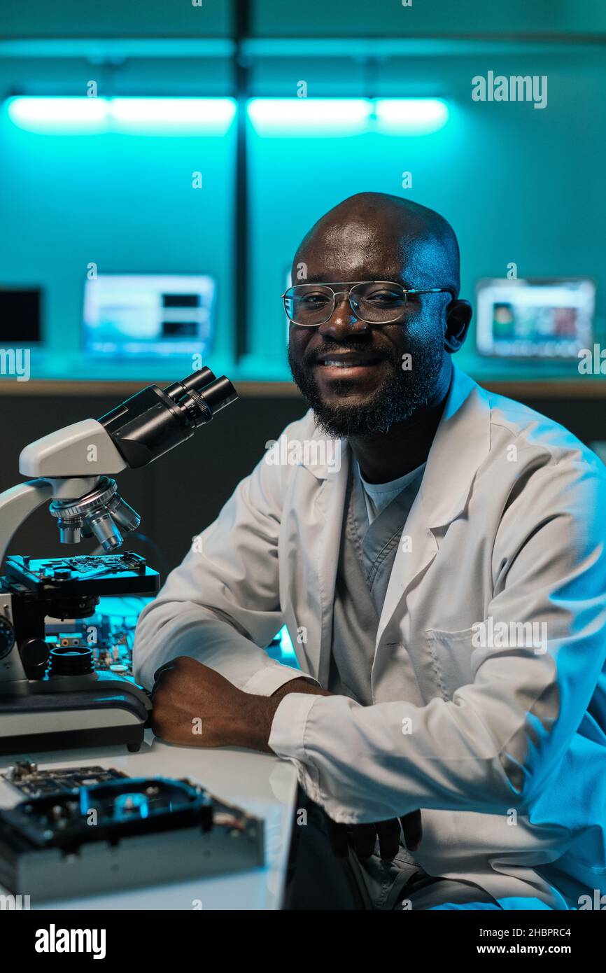 Happy young male laboratory worker in whitecoat and eyeglasses sitting ...