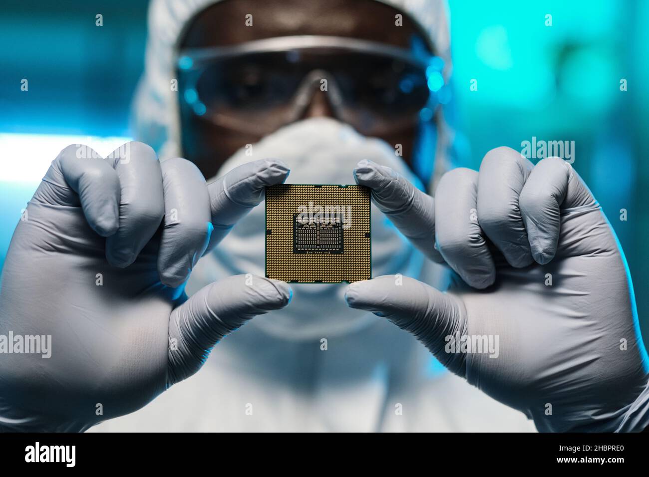 Gloved hands of African man in protective coveralls showing you microchip while holding it in front of camera Stock Photo