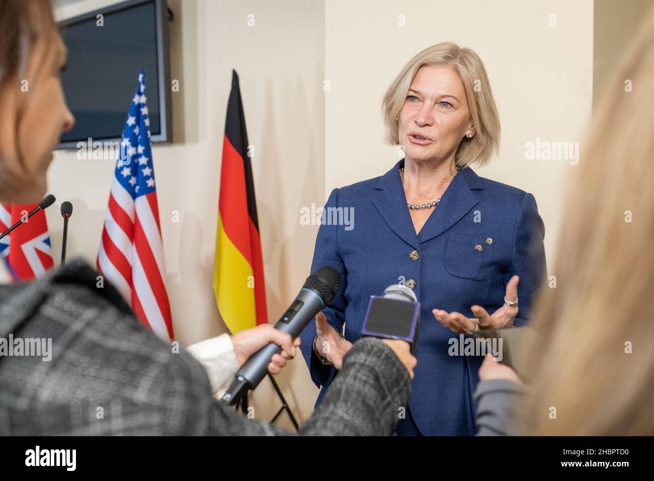 Contemporary female politician in formalwear giving interview to journalists at press conference against national flags Stock Photo
