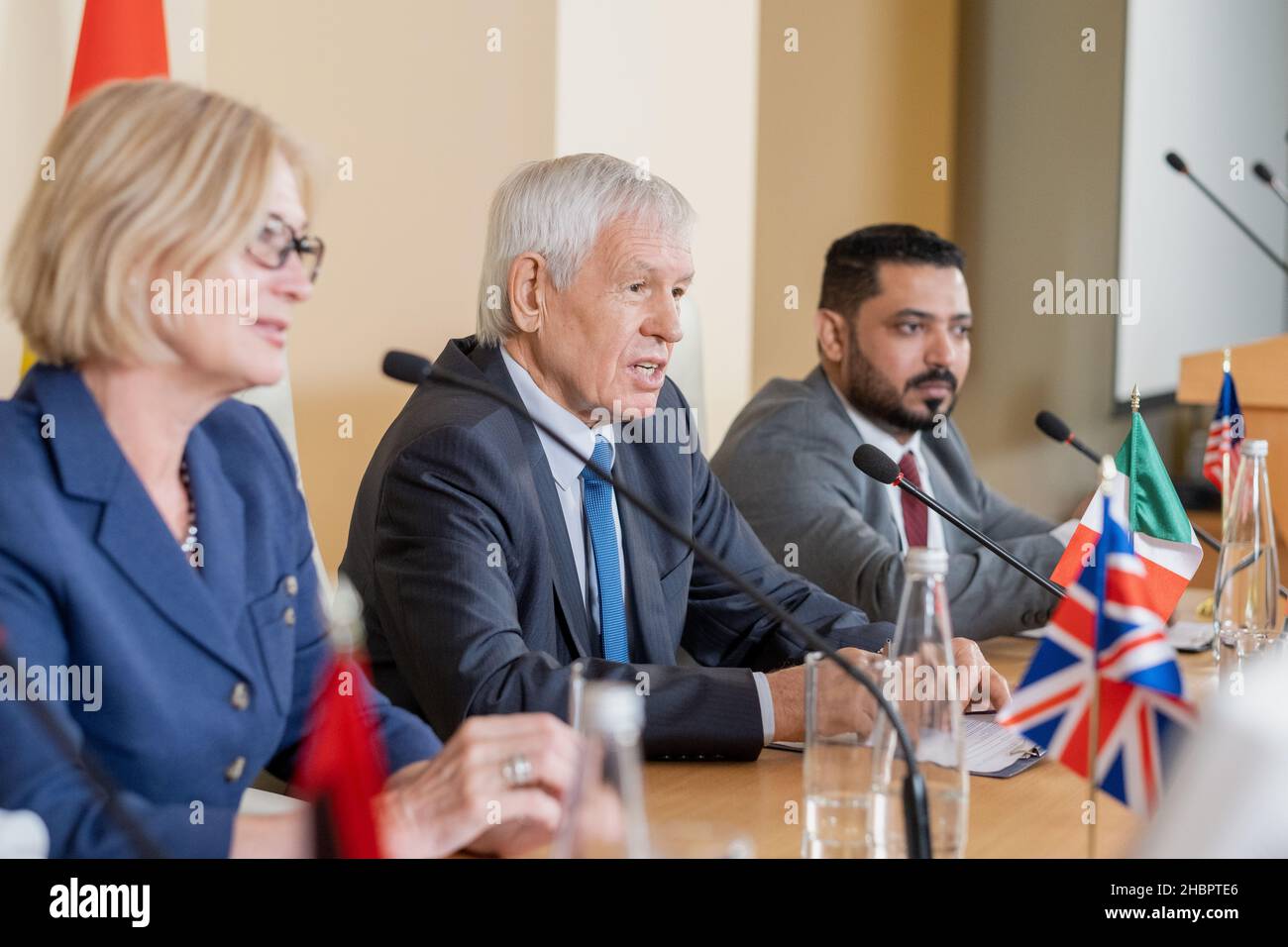Confident senior politician in formalwear speaking at conference while sitting among his colleagues from foreign countries Stock Photo