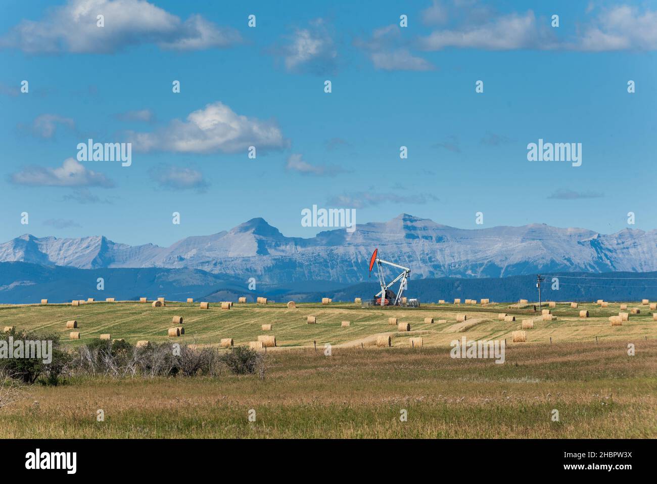 Oil derrick pump among haybales, and farmfeilds in the foothills of Alberta Canada Stock Photo