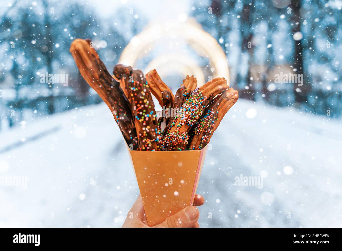 Churros waffles in a hand on the winter snow market. Churros Mexican street food dessert. Fast food sweets, Christmas fair cookies. High quality photo Stock Photo