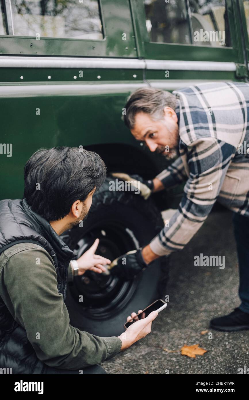 Father changing tire while talking with son on driveway Stock Photo
