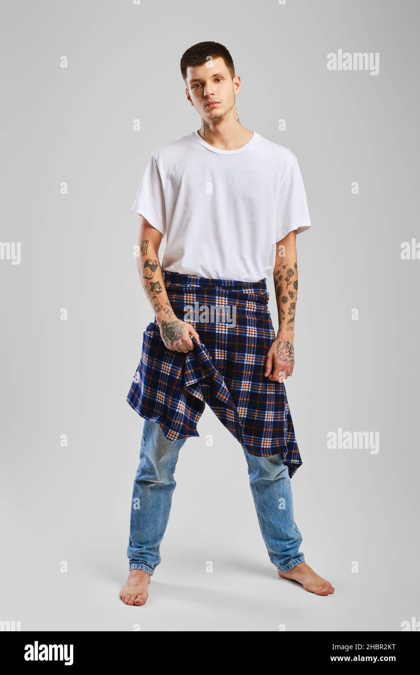 Young cocky man in t-shirt, jeans and checkered shirt tied at the waist Stock Photo