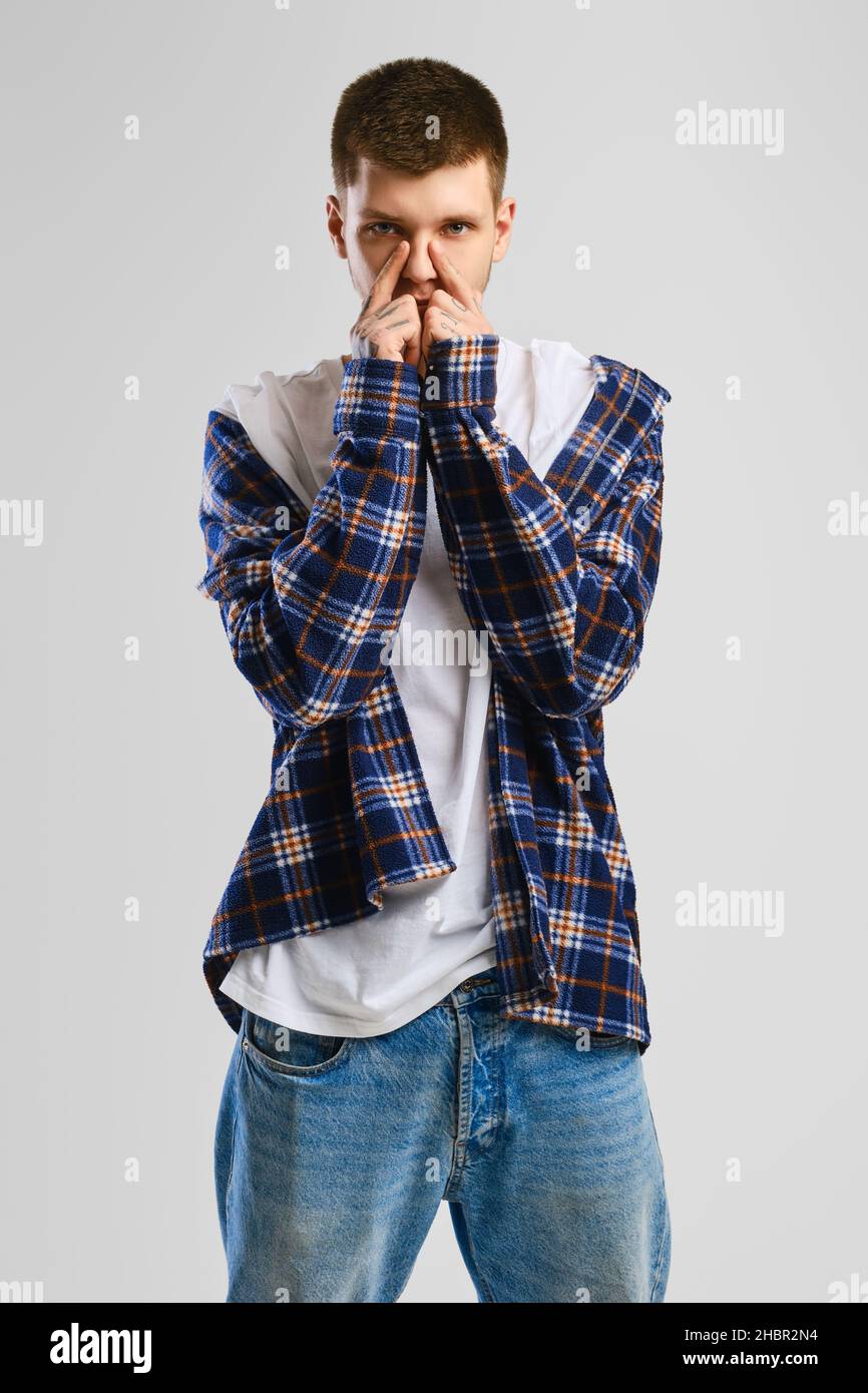 Young cocky man in checkered shirt and jeans touching his nose Stock Photo