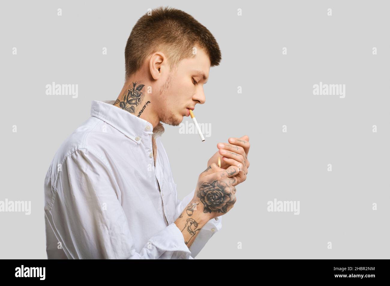 Young tattooed man lights a cigarette in the studio Stock Photo