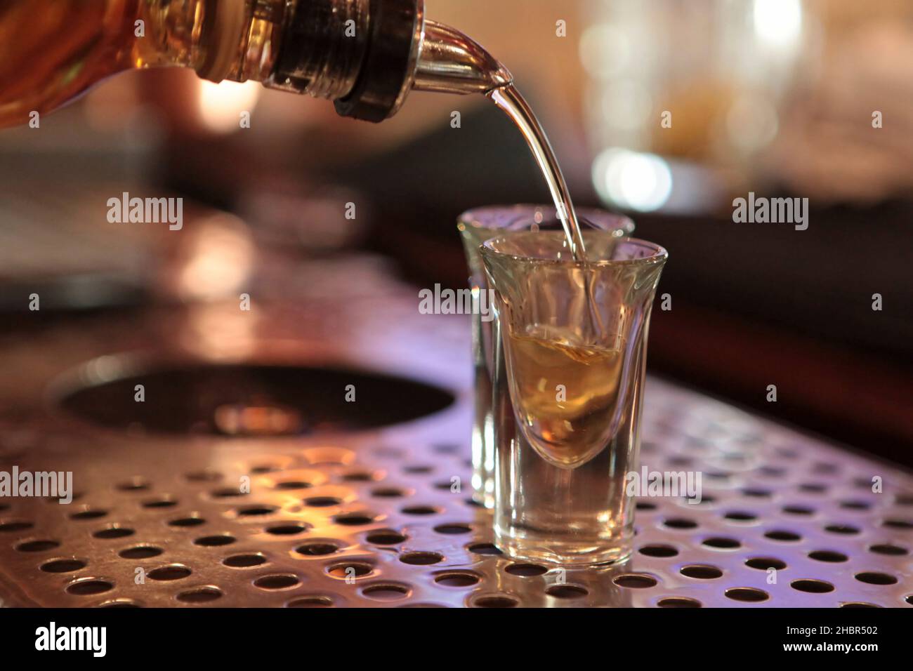Nightlife concept pouring alcohol into two shot glasses on a bar counter Stock Photo