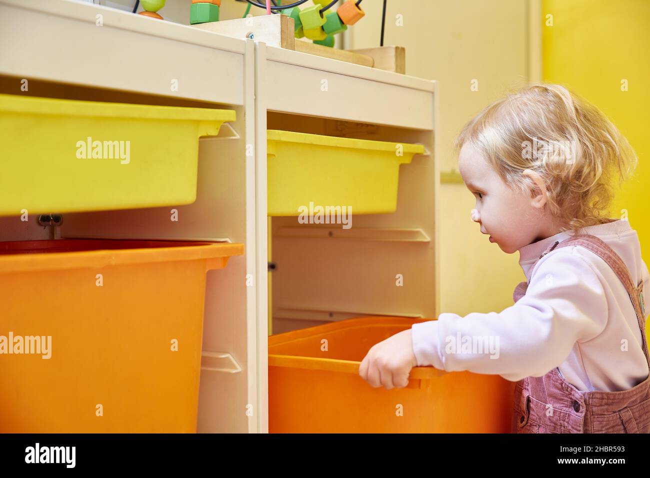 Toy storage system. The child puts the color box in the rack. Stock Photo