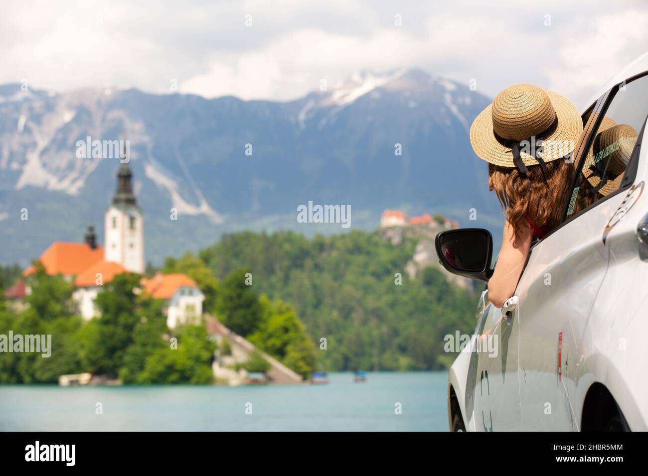 Happy young woman on vacation leaning out of car window on shore of Bled lake, country of Slovenia. Travel, holiday, tourism, explore, rent a car Stock Photo