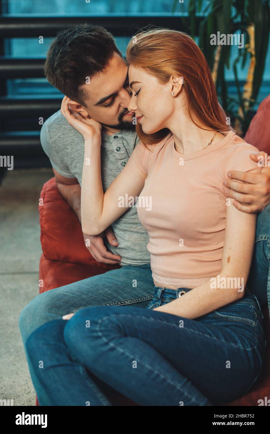 Portrait of a caucasian man kissing red heared woman while sitting on armchair. Affectionate female. Relationships. Stock Photo