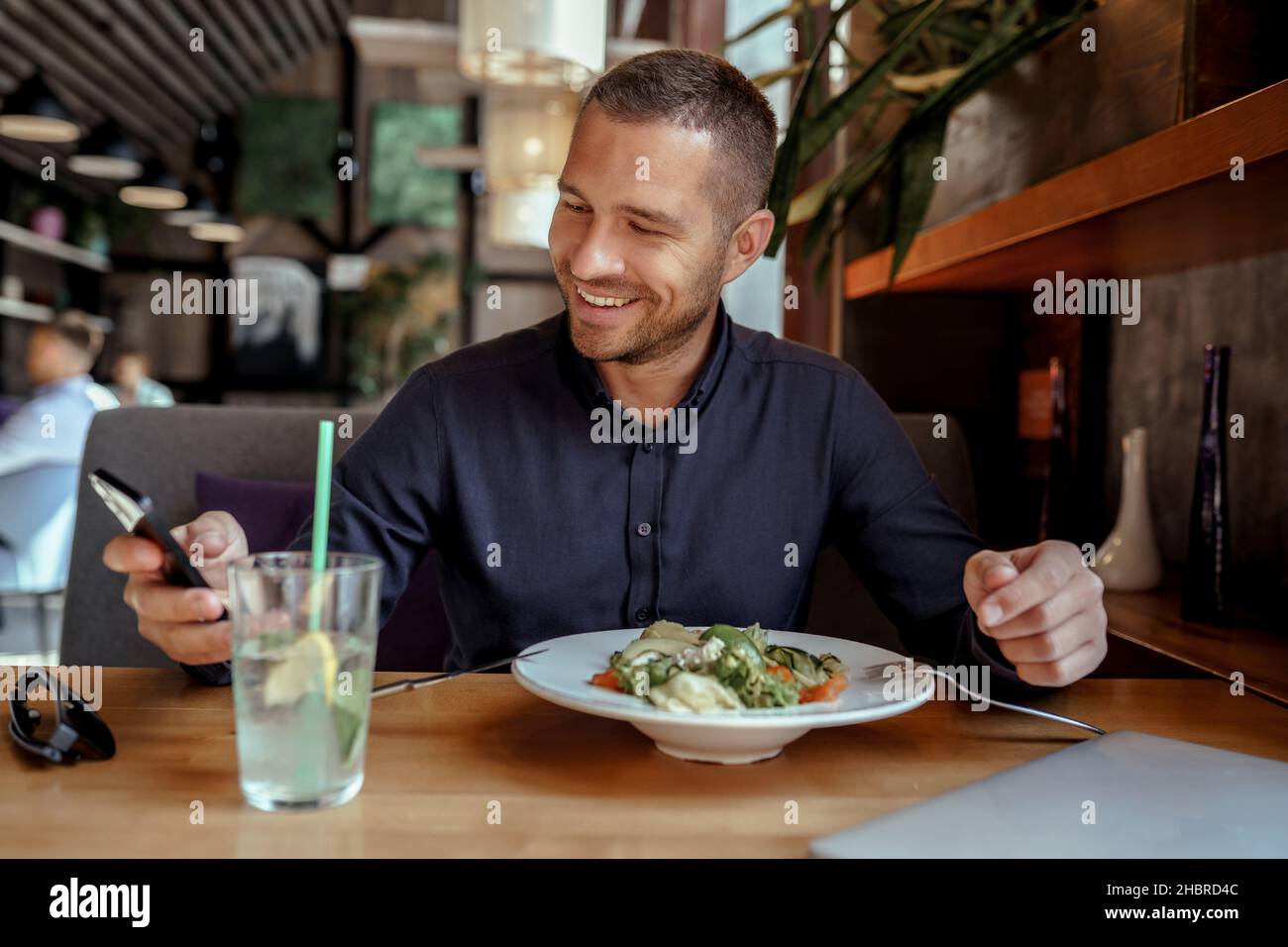 Smiling businessman is using his phone while having lunch in restaurant Stock Photo