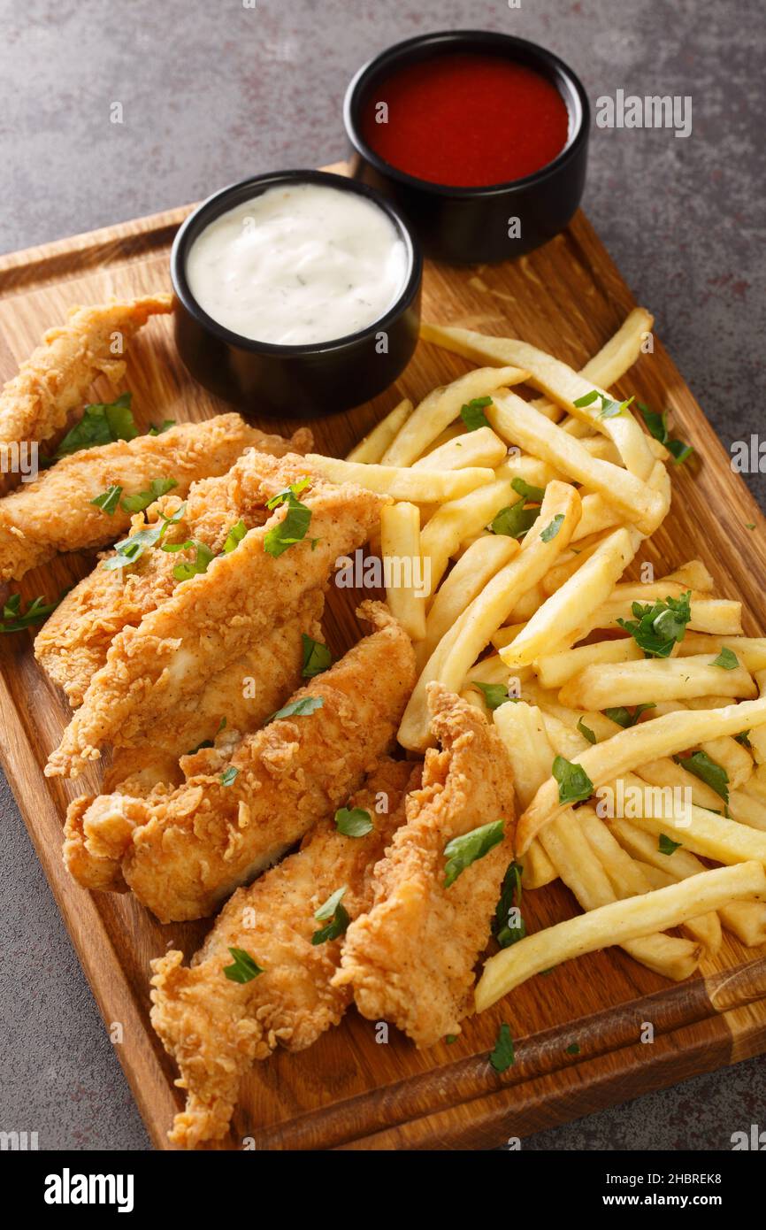 Chicken strips in cornflakes breadcrumb served with french fries sauce closeup on the wooden tray. Vertical Stock Photo
