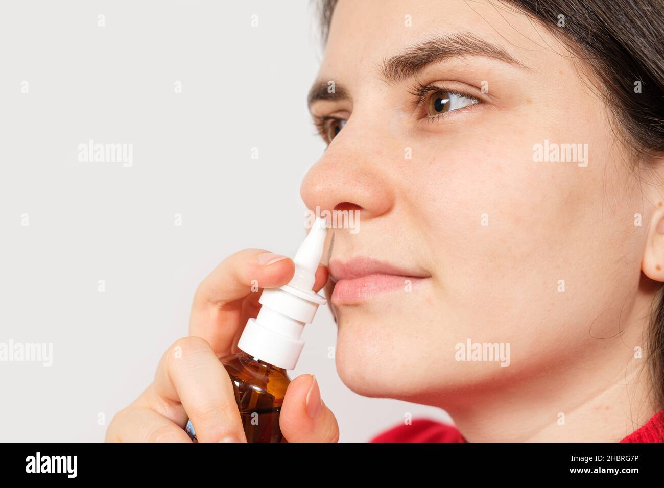 A female patient shoves a spray into the nose to treat rhinitis, an allergy with difficulty breathing. Copy text space. Stock Photo
