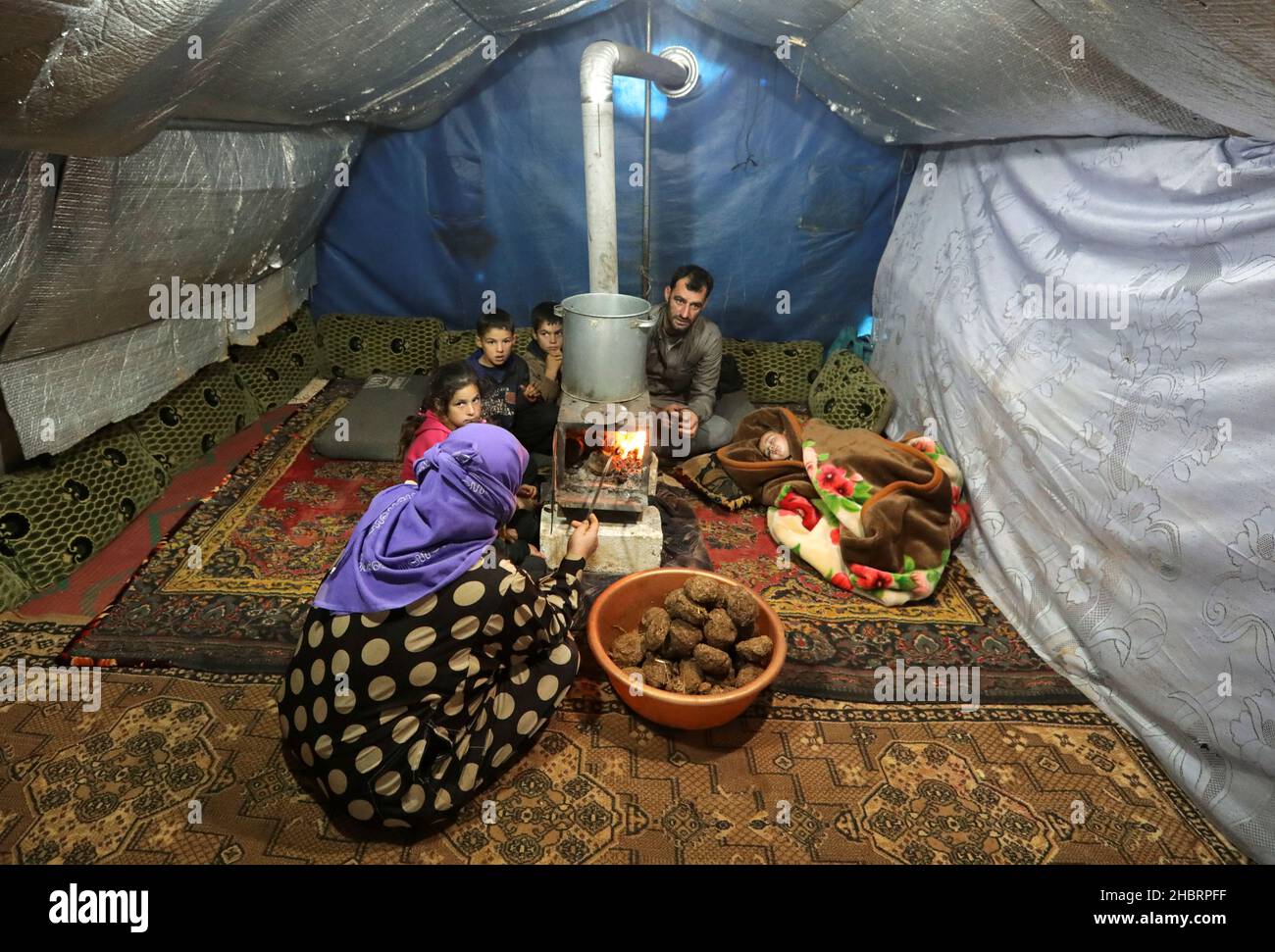 Khaled Muhammad al-Hamadin, a resident of Kafu Arouk camp for internally displaced, sits with his family inside a tent in Idlib, Syria December 20, 2021. Picture taken December 20, 2021. REUTERS/Khalil Ashawi Stock Photo