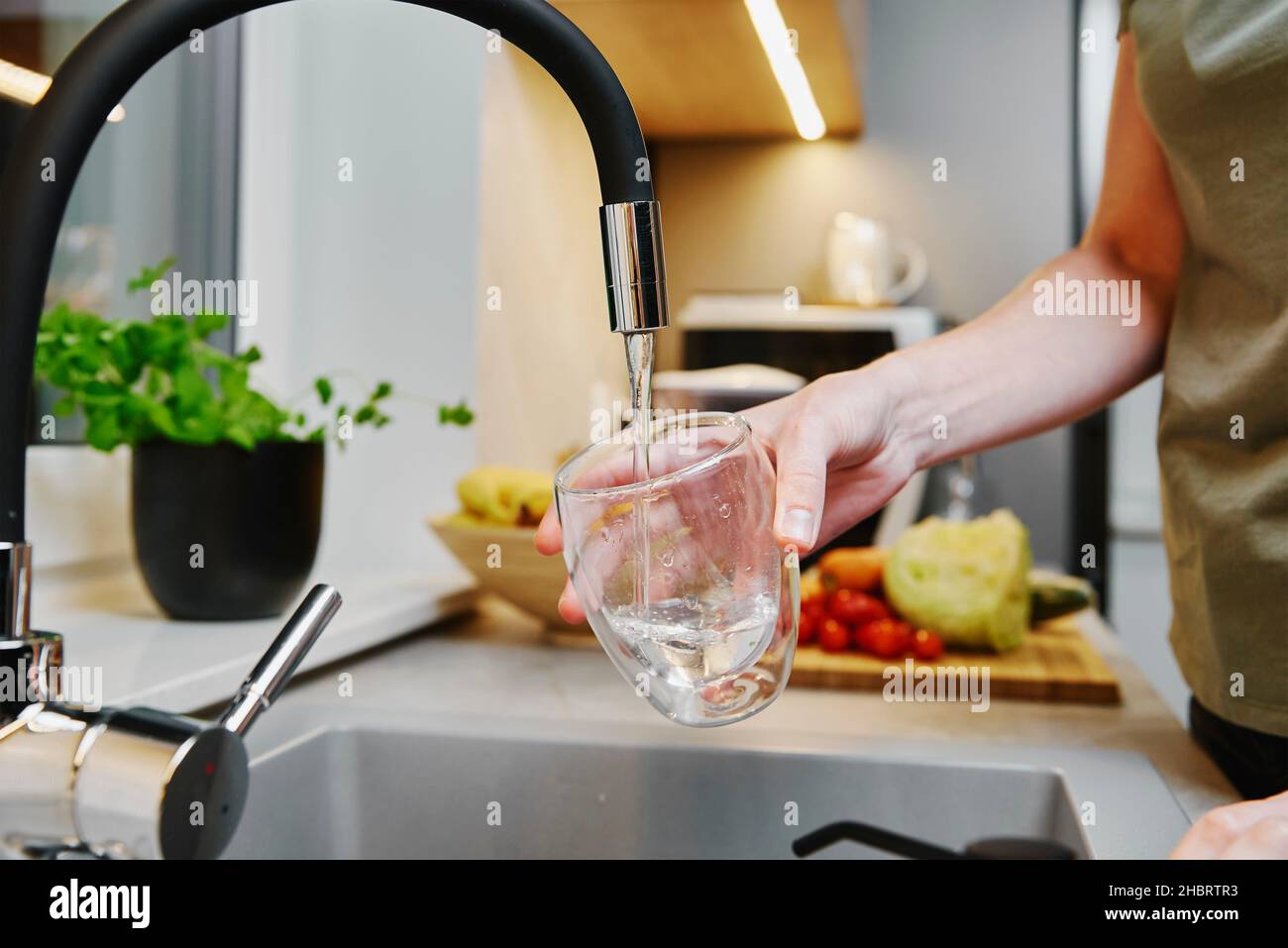 Woman pouring water from faucet into glass at the kitchen Stock Photo