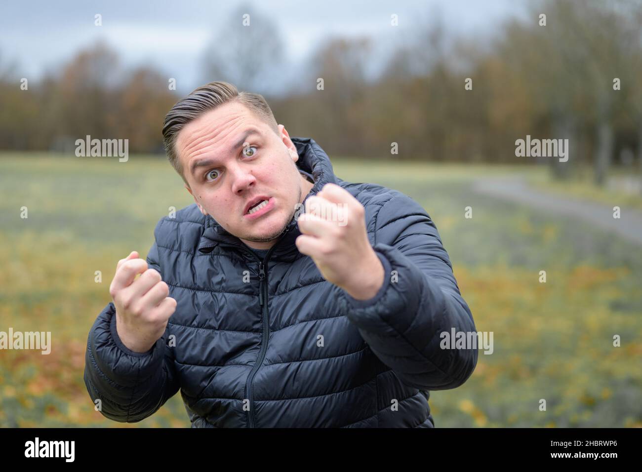 Aggressive angry young man threatening the camera with raised clenched fists as he snarls in fury outdoors in a park Stock Photo