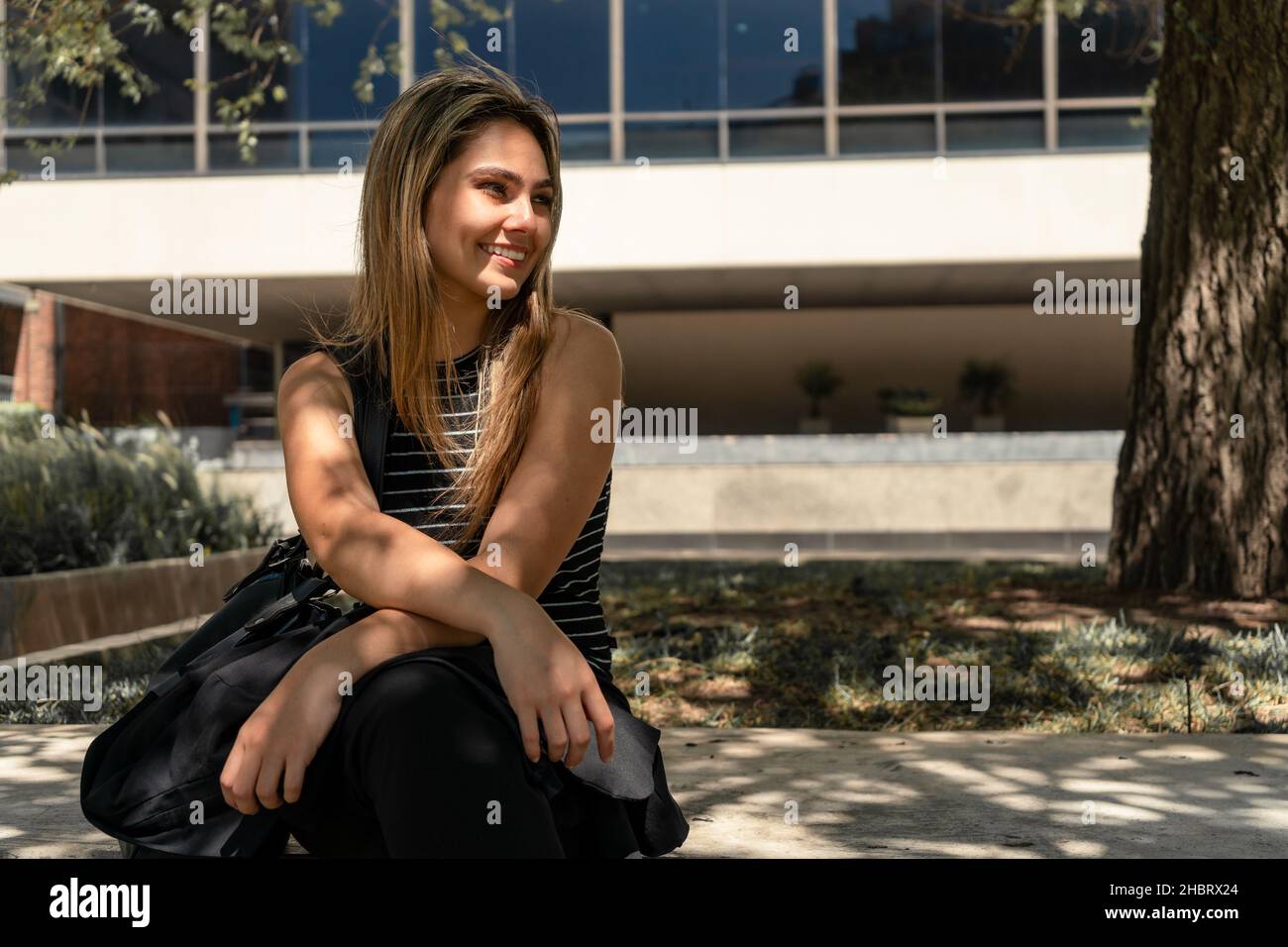 A portrait of a beautiful young smiling woman sitting on a bench in the ...