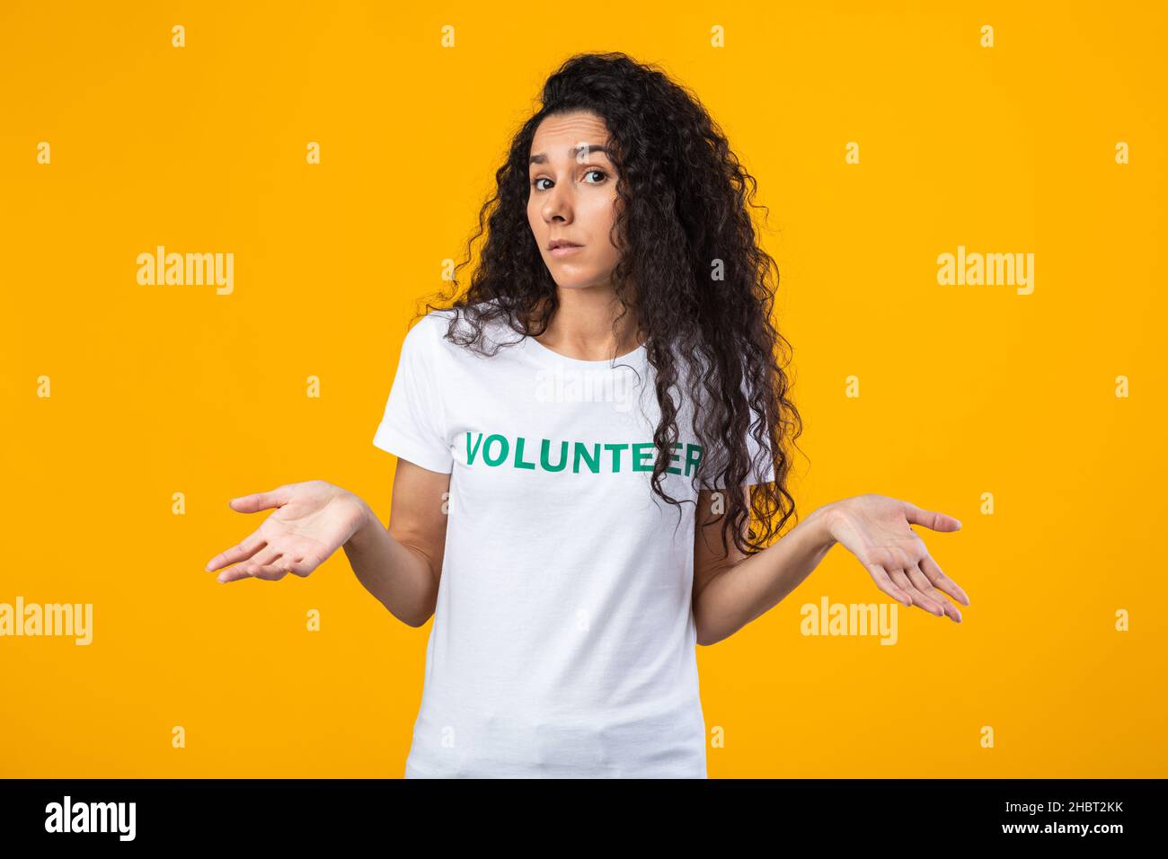 Puzzled Female Volunteer Shrugging Shoulders Posing On Yellow Background Stock Photo