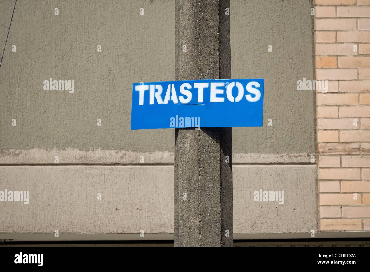 Blue Rectangular Sign that Reads 'Trasteo' (Moving) against a Concrete and Brick Wall Stock Photo