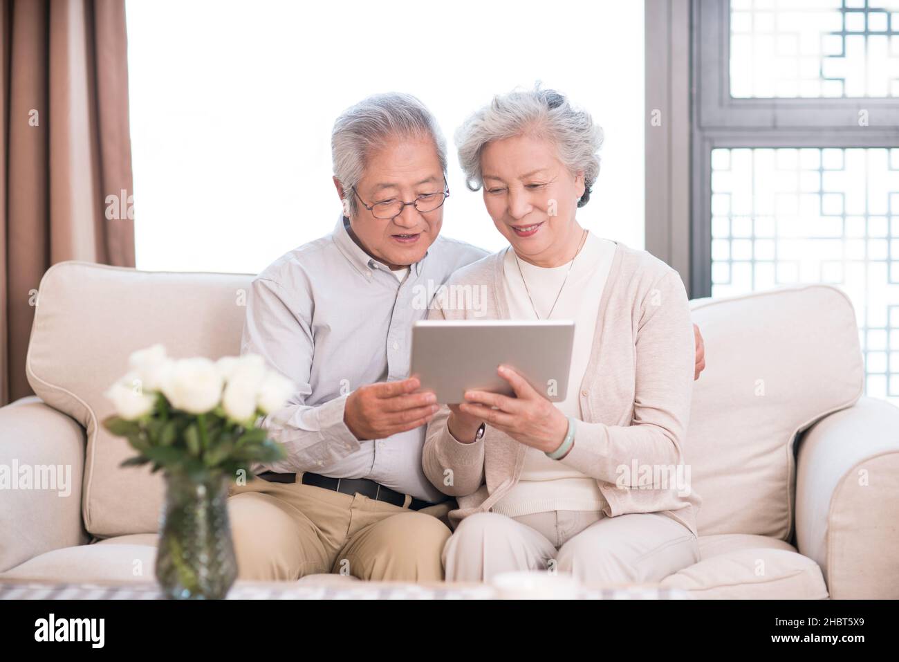 Happy old couple sitting on the sofa and using a tablet computer Stock Photo