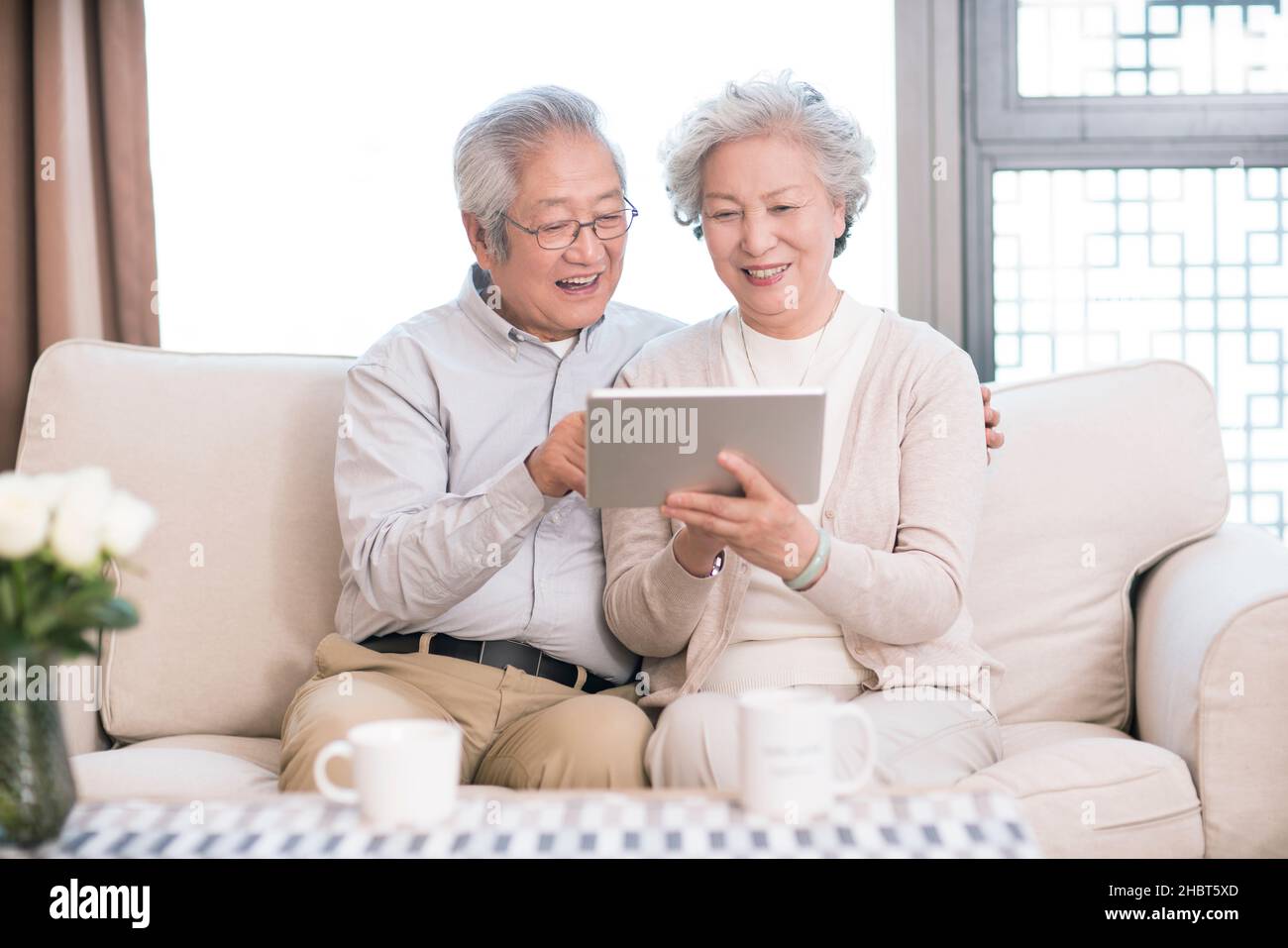 Happy old couple sitting on the sofa and using a tablet computer Stock Photo