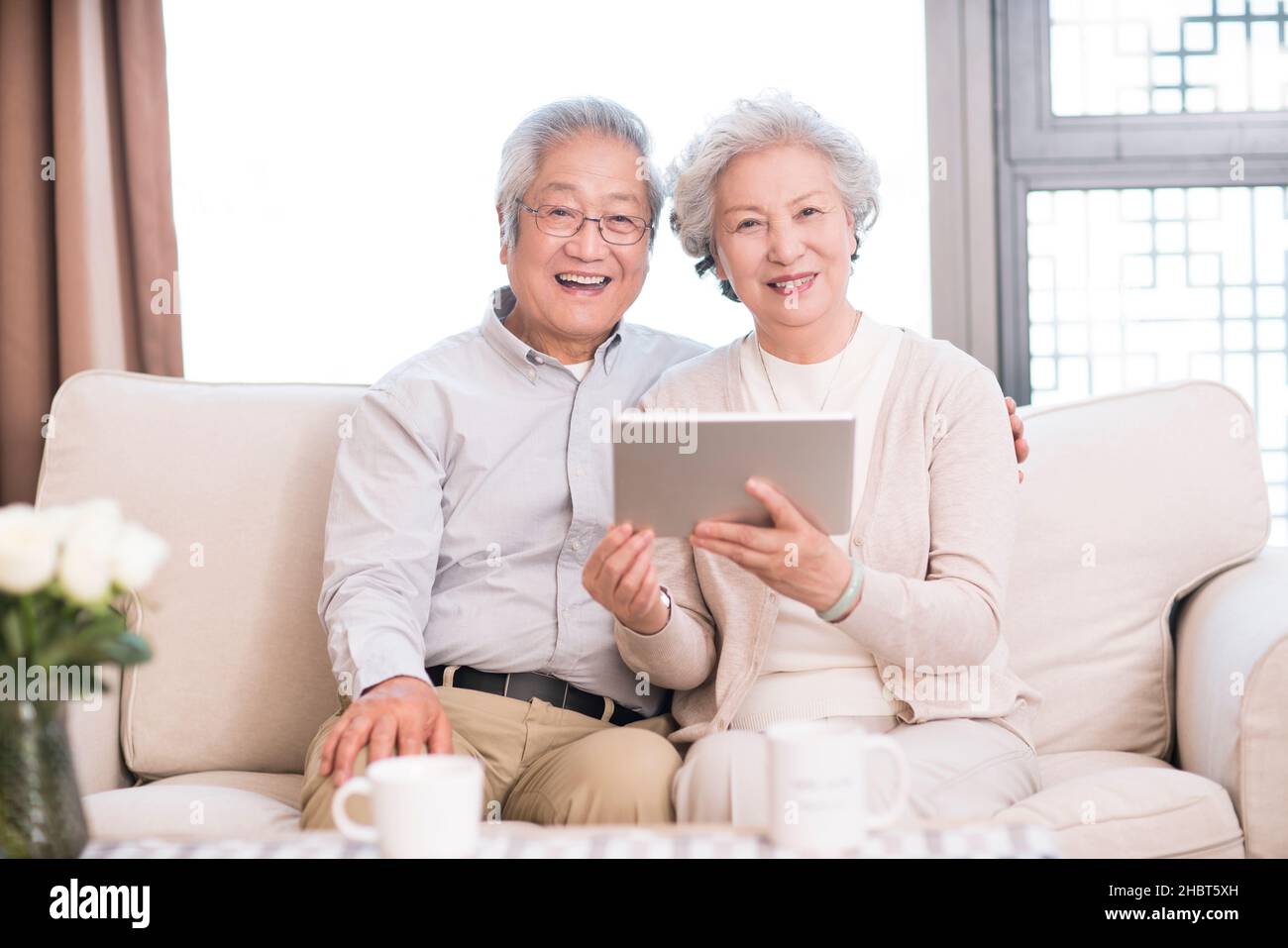 Happy old couple sitting on the sofa and using a tablet computer Stock Photo
