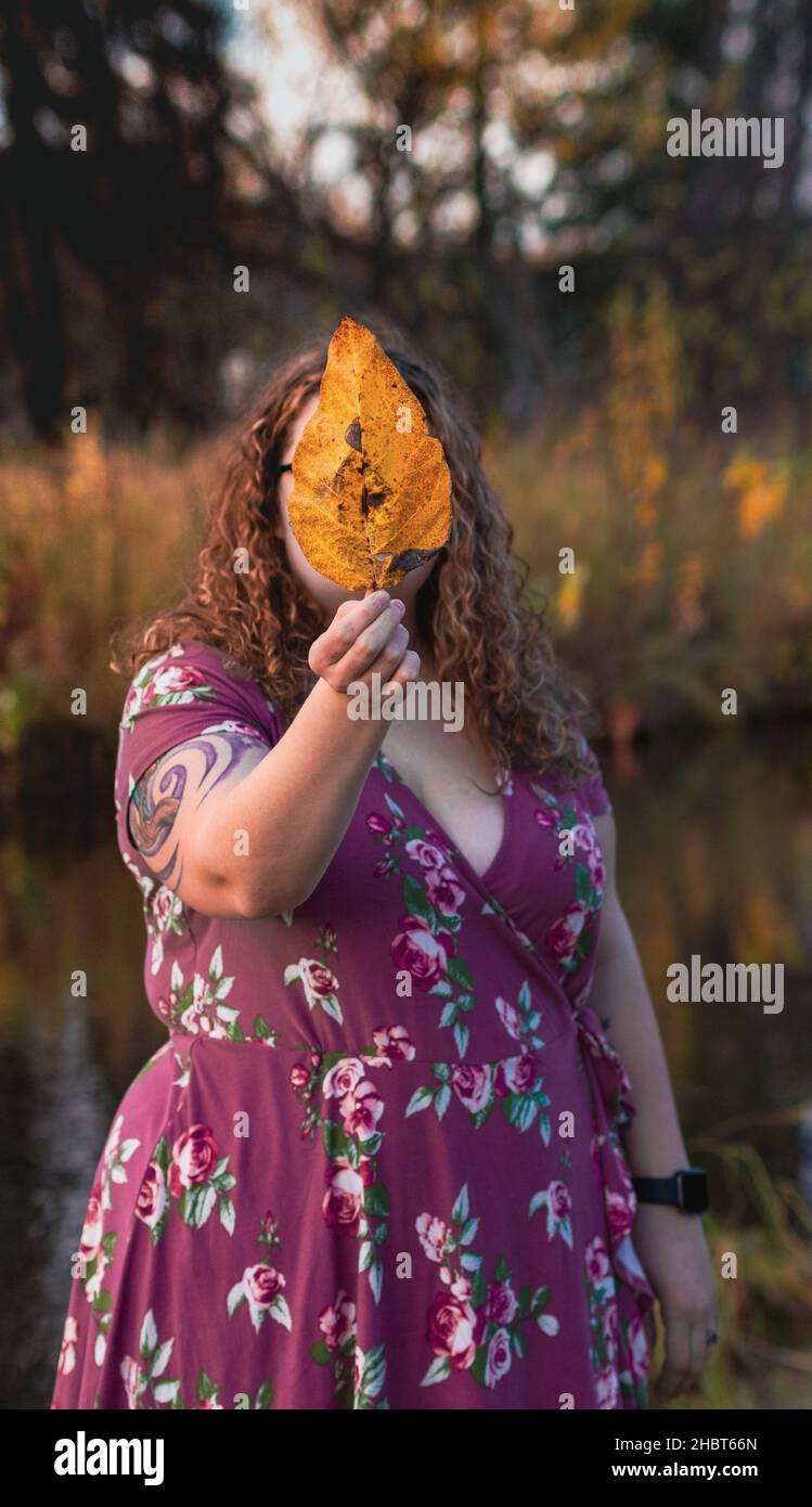 A vertical shot of a young female holding a leaf in front of her face ...