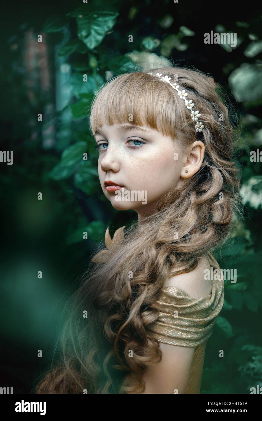 girl of 9-12 years old - with the appearance of a princess with long hair, in a thicket of hydrangeas. beautiful arrogant and serious girl among flowe Stock Photo