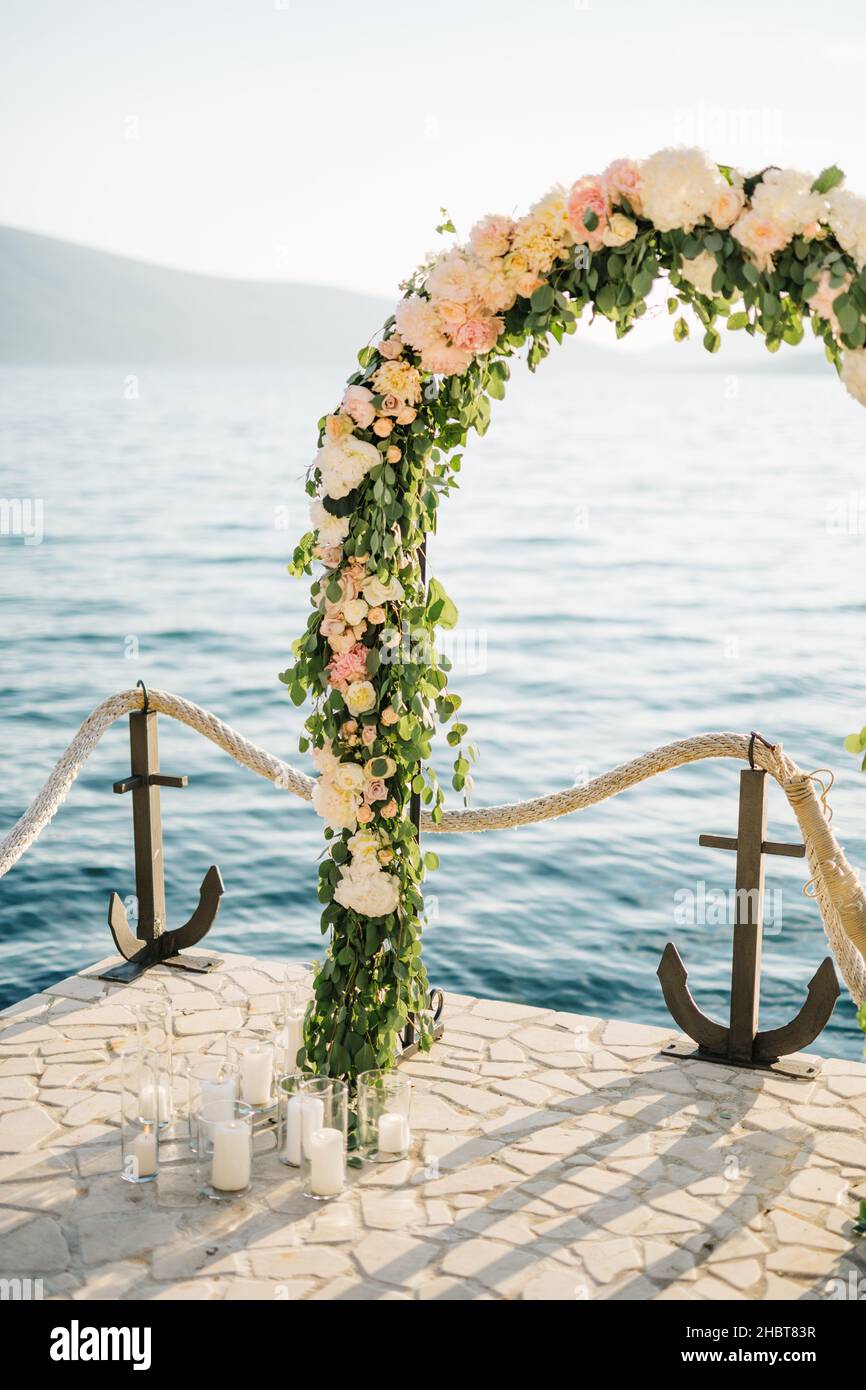 Wedding arch stands on a cobbled pier by a rope fence with anchors