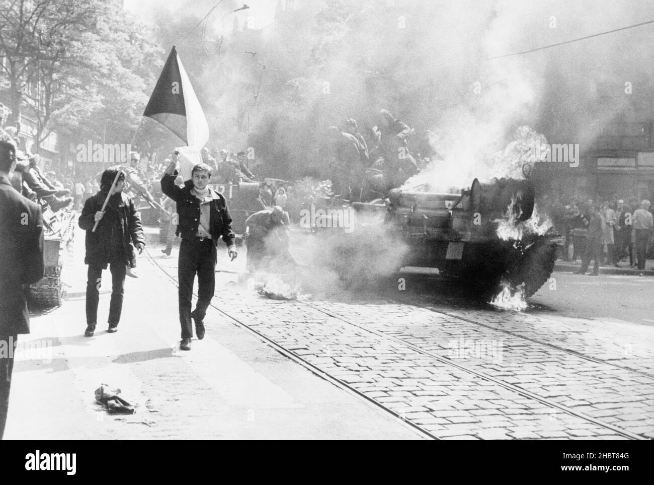 During the Soviet invasion of Czechoslovakia, Czechoslovaks carry their national flag past a burning tank in Prague Stock Photo