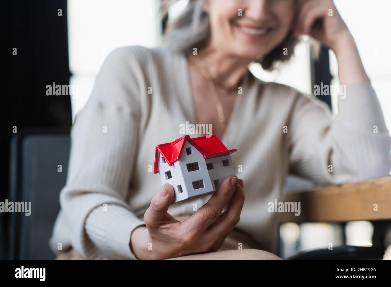 Cropped view of model of house in hand of blurred businesswoman in office Stock Photo