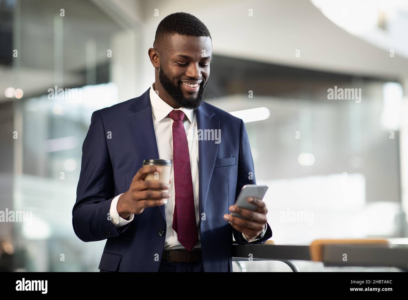 Cheerful black manager drinking coffee, using mobile phone Stock Photo
