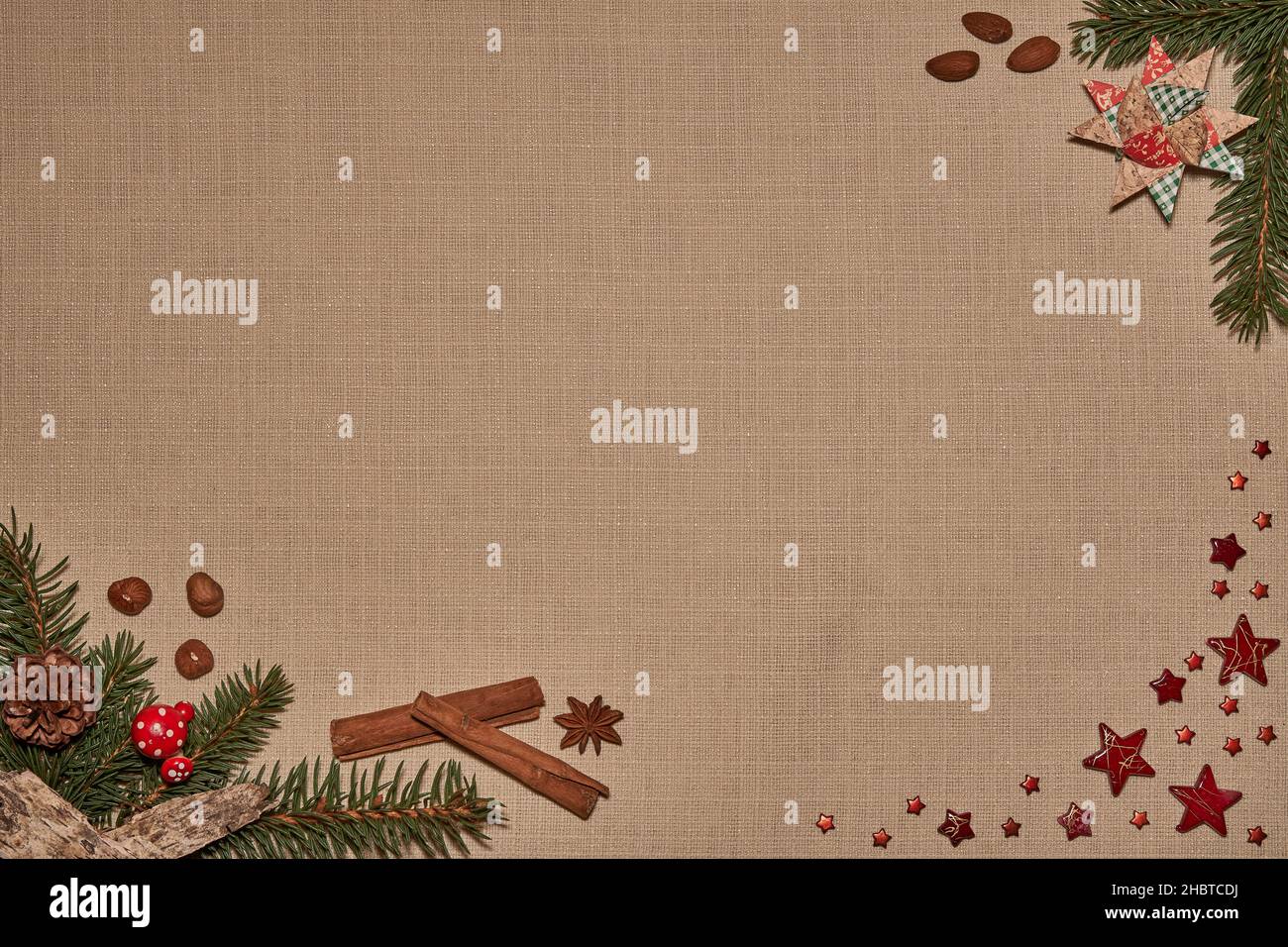 Weihnachtliches Hintergrundmotiv mit Tannenzweigen, Sternen, Nüssen, Mandeln und Gewürzen auf Textilgewebe Stock Photo