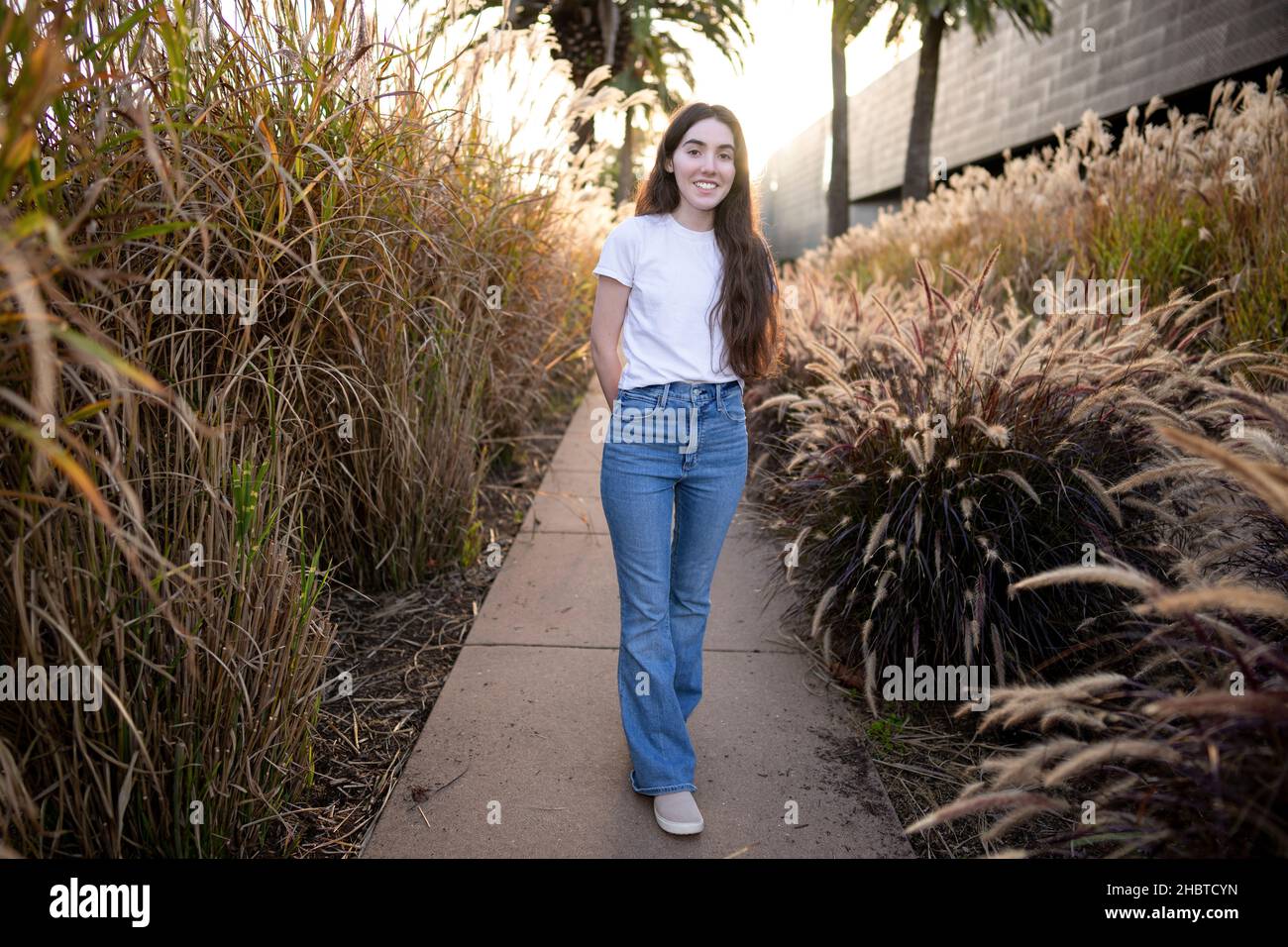 Teenage Woman Standing in Walkway Surrounded by Fountain Grass Stock Photo