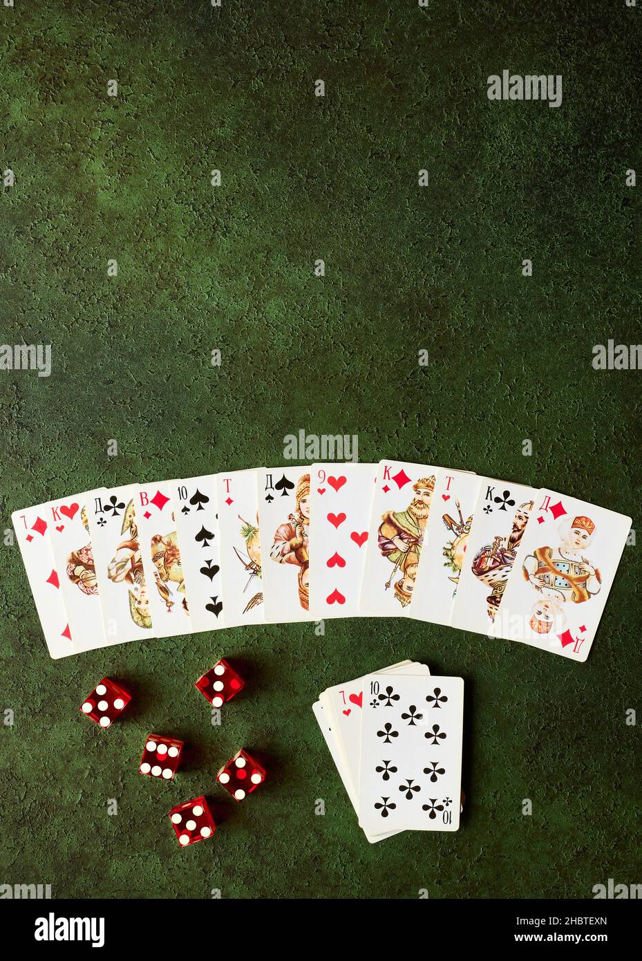 Decomposed deck of playing cards and red dice on green textured background with copy space, gambling concept: Zhukovsky, Russia - December 19, 2021 Stock Photo
