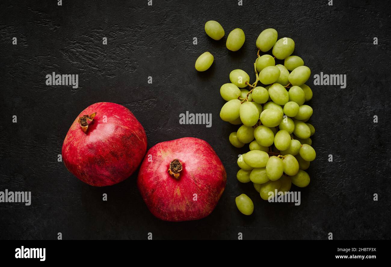 Ripe pomegranates and a bunch of green grapes on dark background space for text Stock Photo