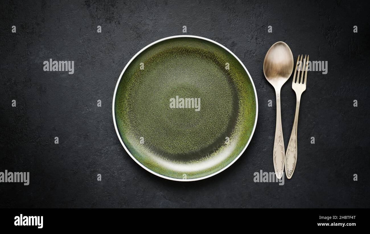 Empty ceramic plate green and old cupronickel spoon and fork on black slate table Stock Photo
