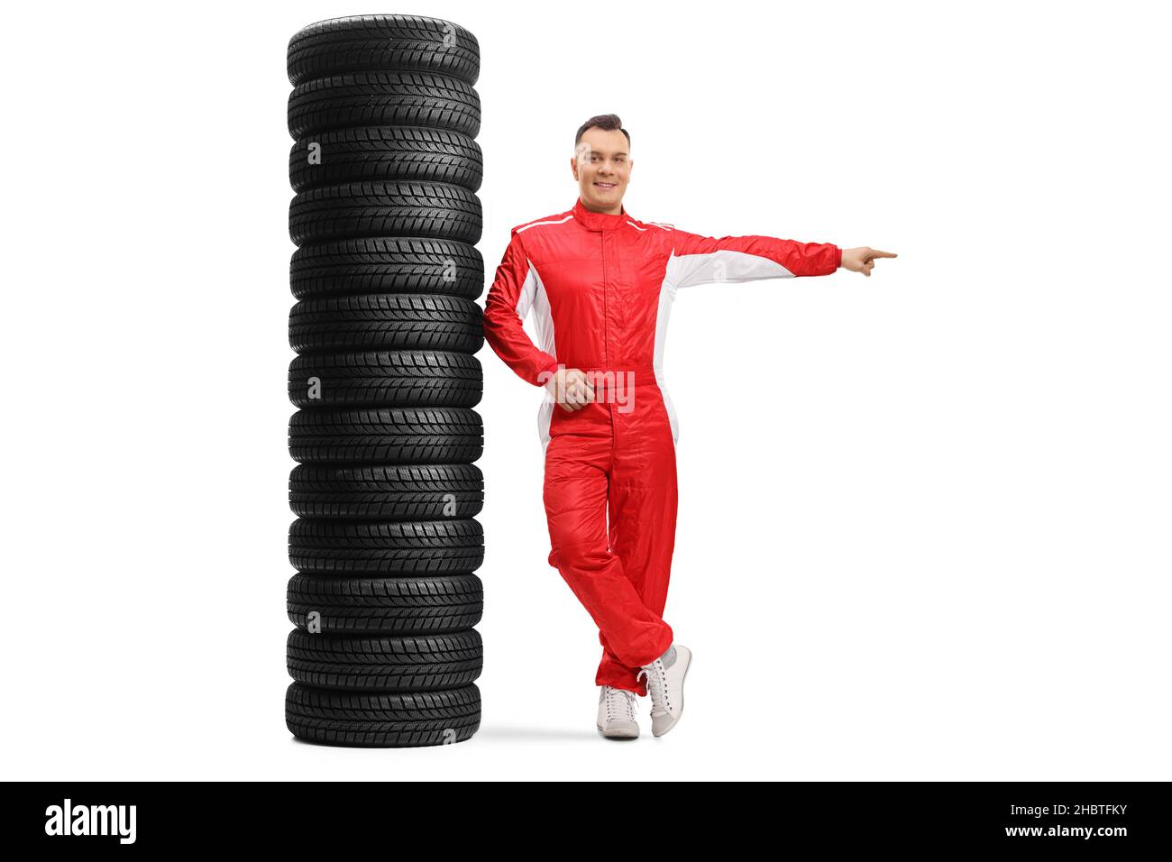 Full length portrait of a racer leaning on a pile of tires and pointing to the side isolated on white background Stock Photo