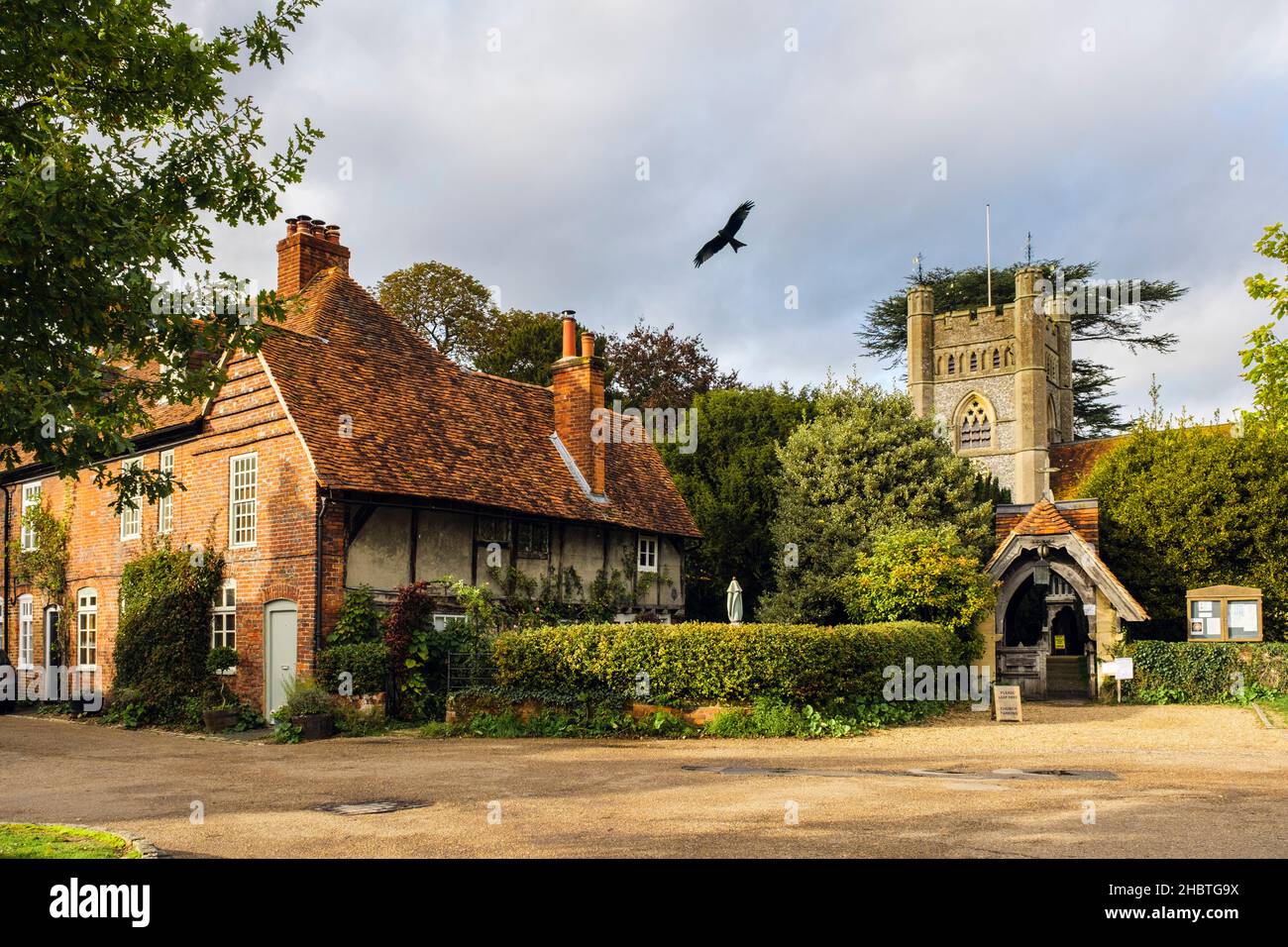 Period cottages by 14c St Mary the Virgin church in historic Chilterns village with Red Kite flying low overhead. Hambleden Buckinghamshire England UK Stock Photo