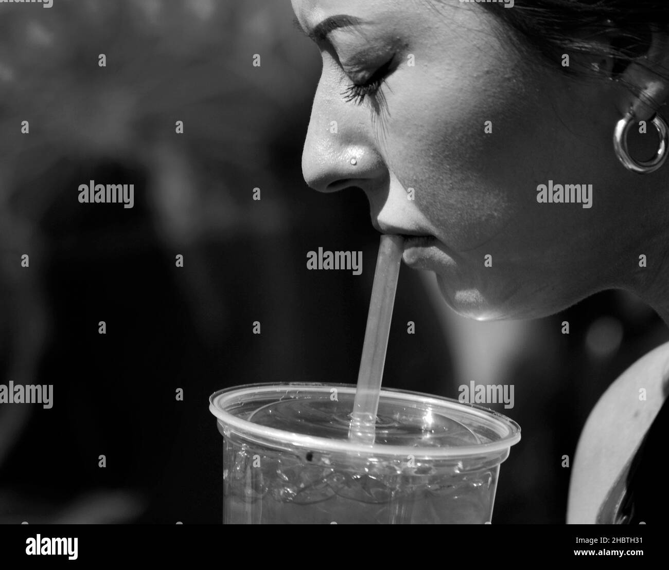 A young woman drinks juice from a plastic container using a plastic straw at a festival in Santa Fe, New Mexico. Stock Photo