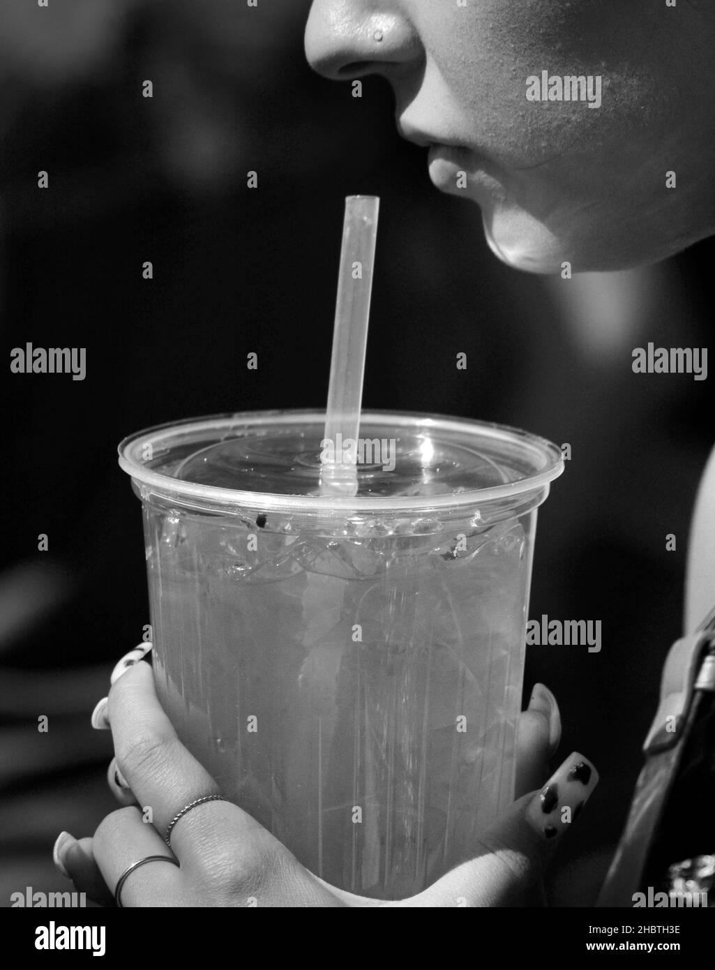 A young woman drinks juice from a plastic container using a plastic straw at a festival in Santa Fe, New Mexico. Stock Photo