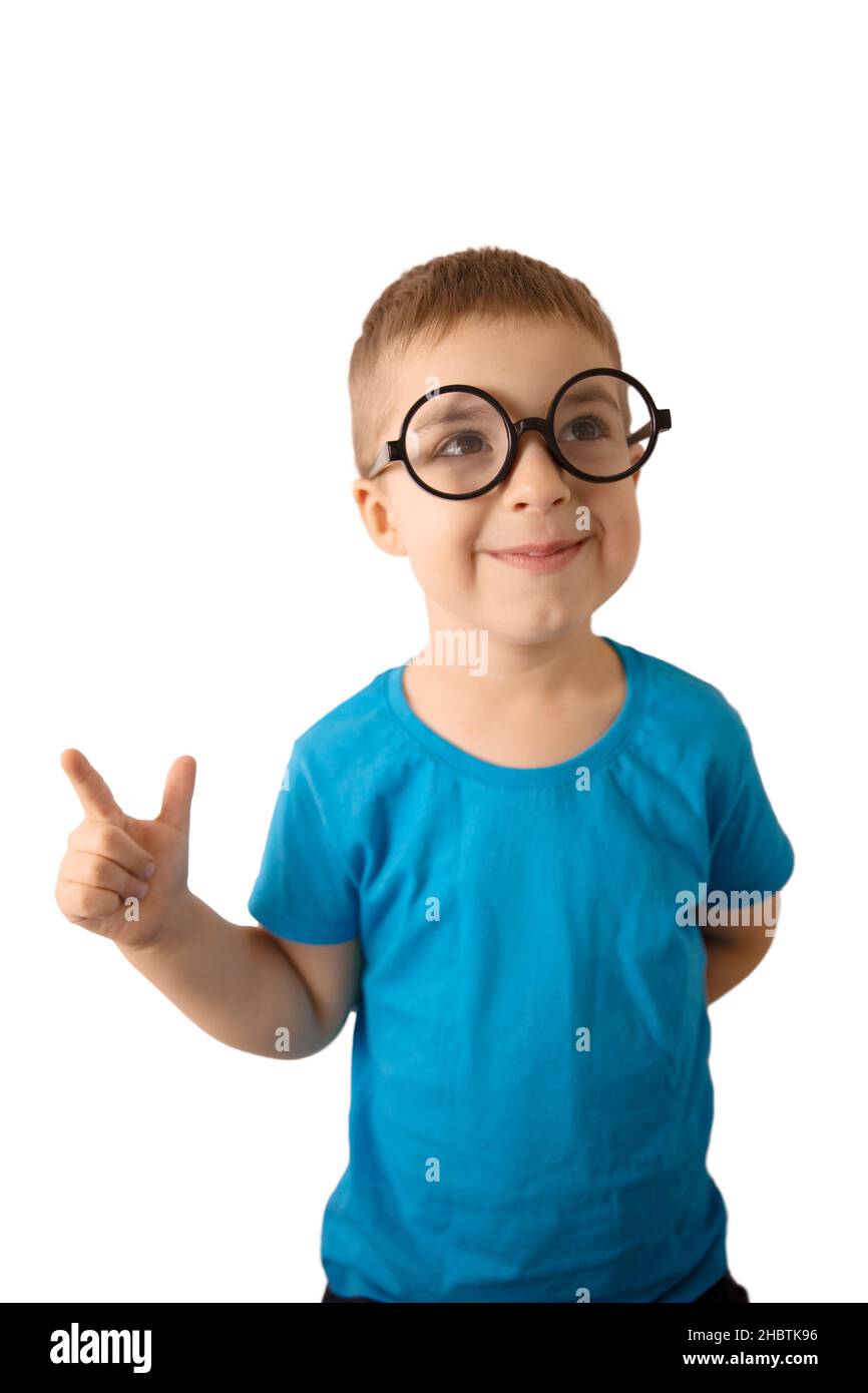 Little caucasian boy with glasses, thinking and showing something with finger, isolated on white background. Smiling child with blue shirt is Stock Photo